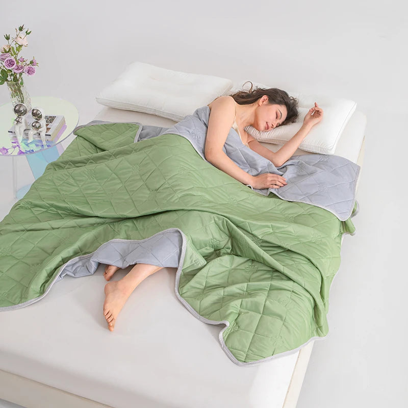 A woman is relaxing on a white surface covered with a green quilted blanket.