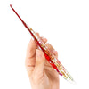 A hand holds a floral patterned epoxy crochet hook set with a red and gold design.
