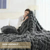 A dark gray faux fur rabbit blanket draped over a bed, emphasizing its fluffy texture and cozy appearance.