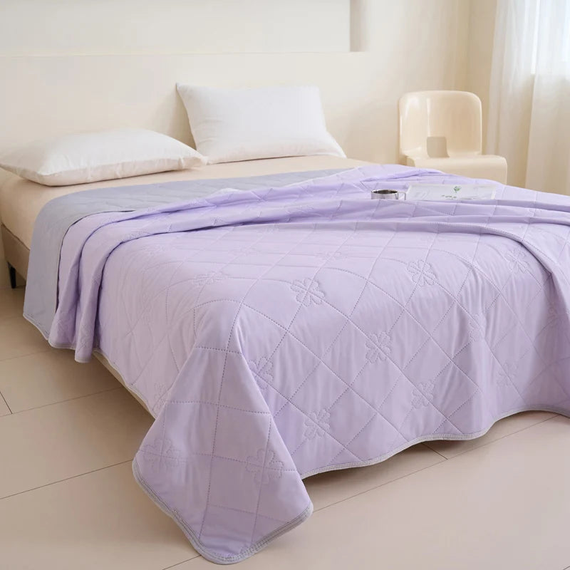 A purple quilted blanket is spread on a bed in a bright room.