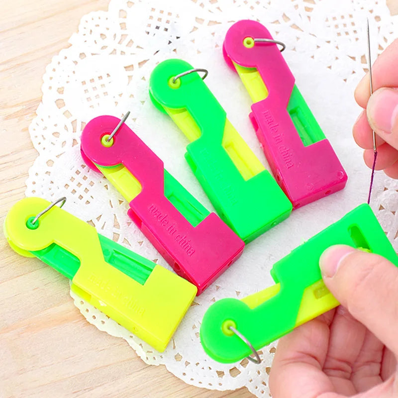 A set of pink and lime green automatic sewing needle threaders resting on a white lace doily.