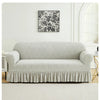 A light gray sofa cover with a ruffled skirt is displayed against a white wall with a black floral print above it.