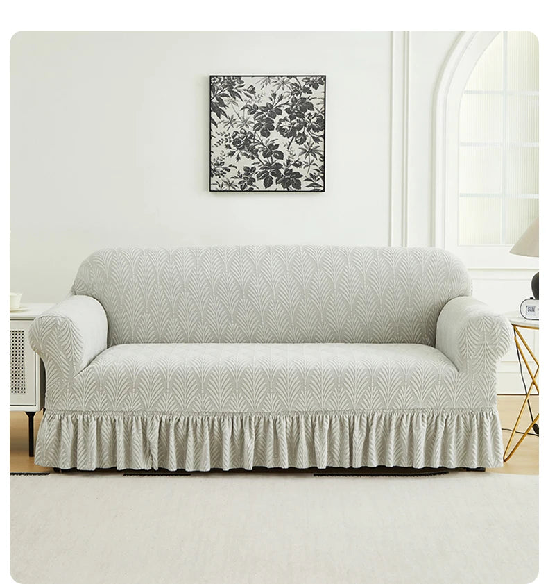 A light gray sofa cover with a ruffled skirt is displayed against a white wall with a black floral print above it.
