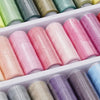 A collection of spools of pink, green, and purple polyester sewing thread in a white plastic tray.
