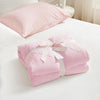 Pink cooling breathable blanket folded and placed on a white bed with a pillow.