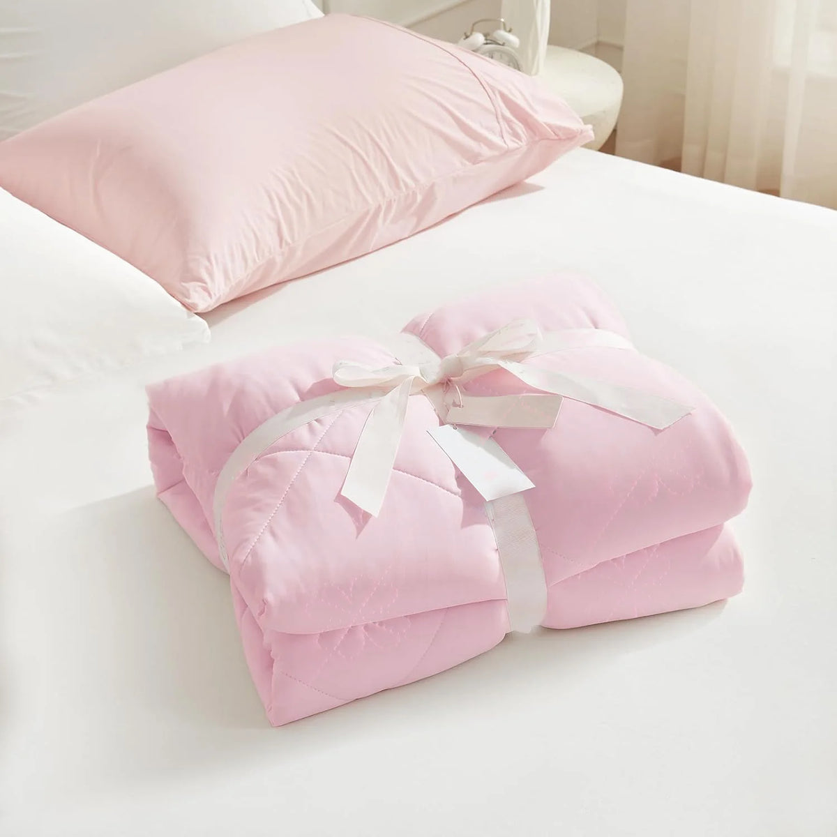 Pink cooling breathable blanket folded and placed on a white bed with a pillow.