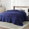 A dark blue faux fur rabbit blanket draped over a bed in a bright room.