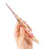 A hand holds a clear epoxy crochet hook with a floral pattern, showing its delicate design.