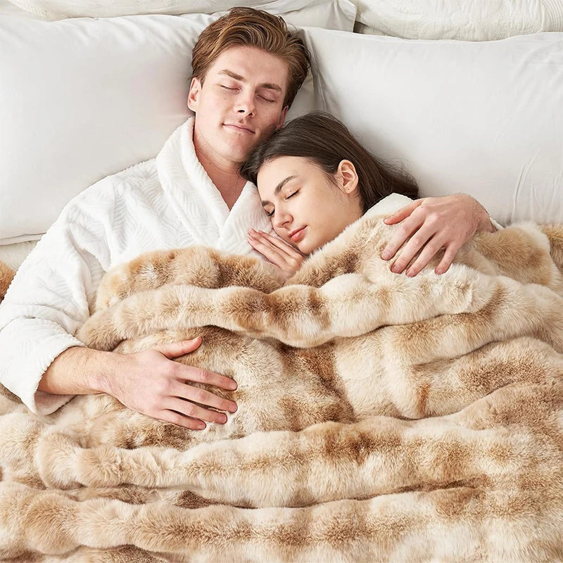 A couple relaxing under a fluffy beige faux fur blanket in bed.