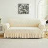 A cream-colored sofa cover with a ruffled skirt sits on a light rug in a bright room above a white cabinet.