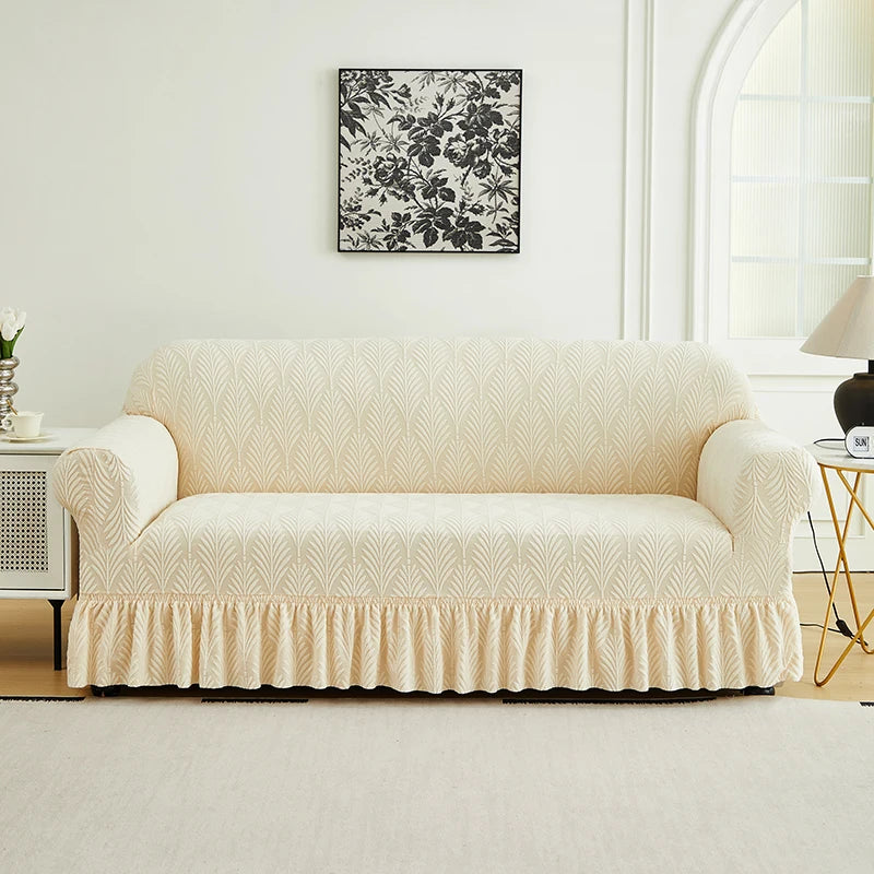 A cream-colored sofa cover with a ruffled skirt sits on a light rug in a bright room above a white cabinet.