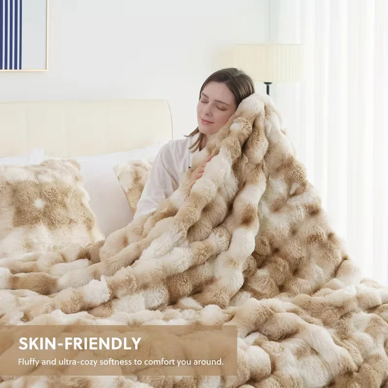 A woman is wrapped in a fluffy, light brown faux fur blanket indoors.