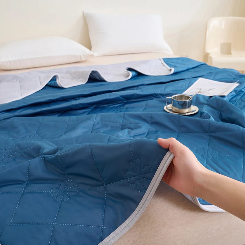 A hand folds a blue quilted blanket on a bed, showing its texture and stitching.