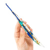 A hand holds a long, slender epoxy crochet hook with a floral pattern in blue and gold.