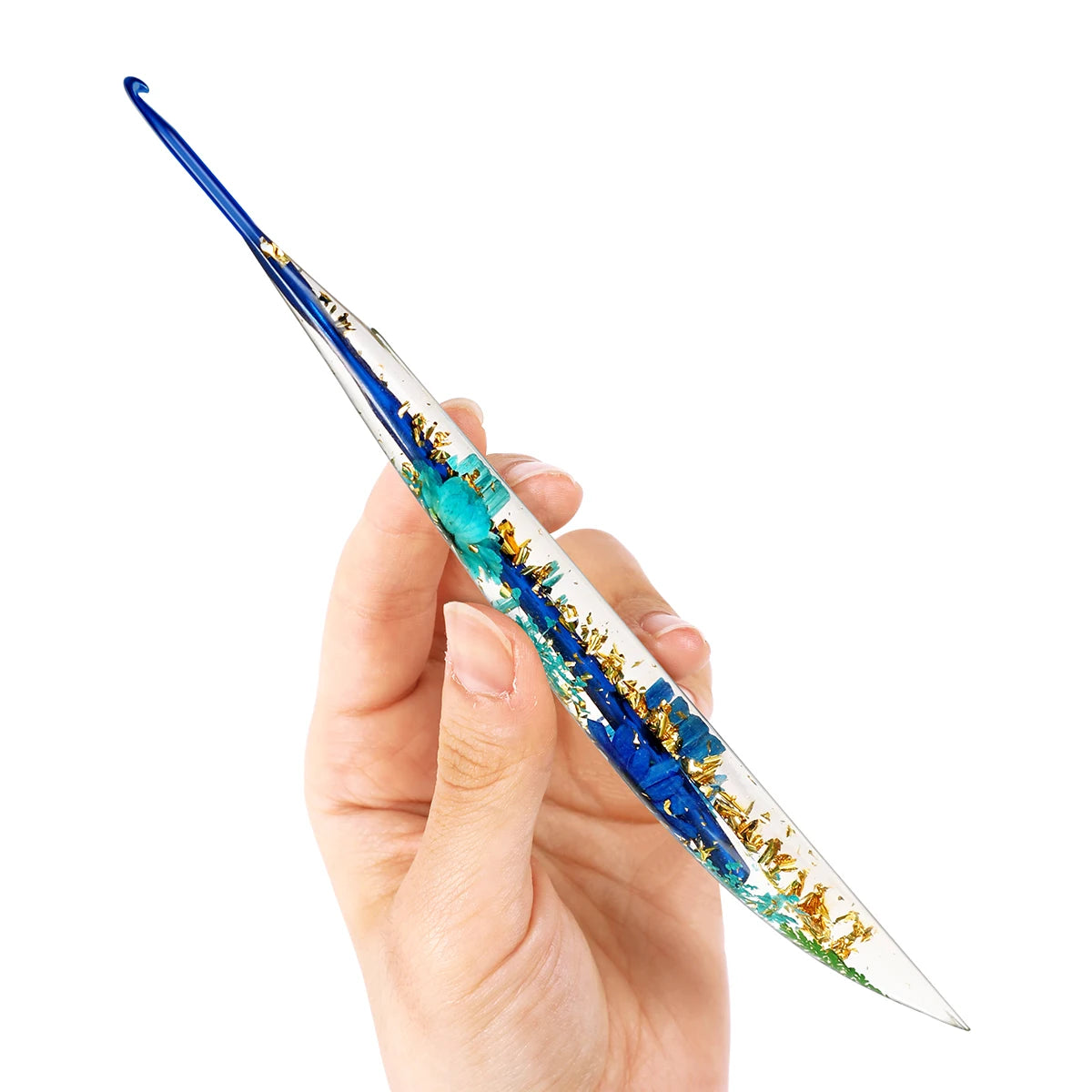 A hand holds a long, slender epoxy crochet hook with a floral pattern in blue and gold.