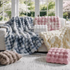 A collection of oversized plush faux fur bubble blankets in shades of blue, pink, and cream displayed on a light-colored floo