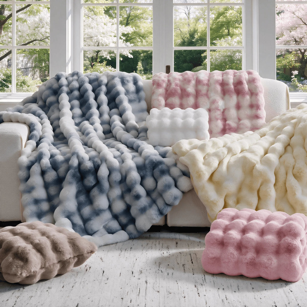A collection of oversized plush faux fur bubble blankets in shades of blue, pink, and cream displayed on a light-colored floo