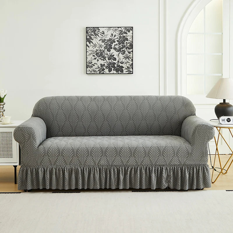 A gray sofa cover with a ruffled skirt is displayed against a white wall, above a framed black and white floral print.