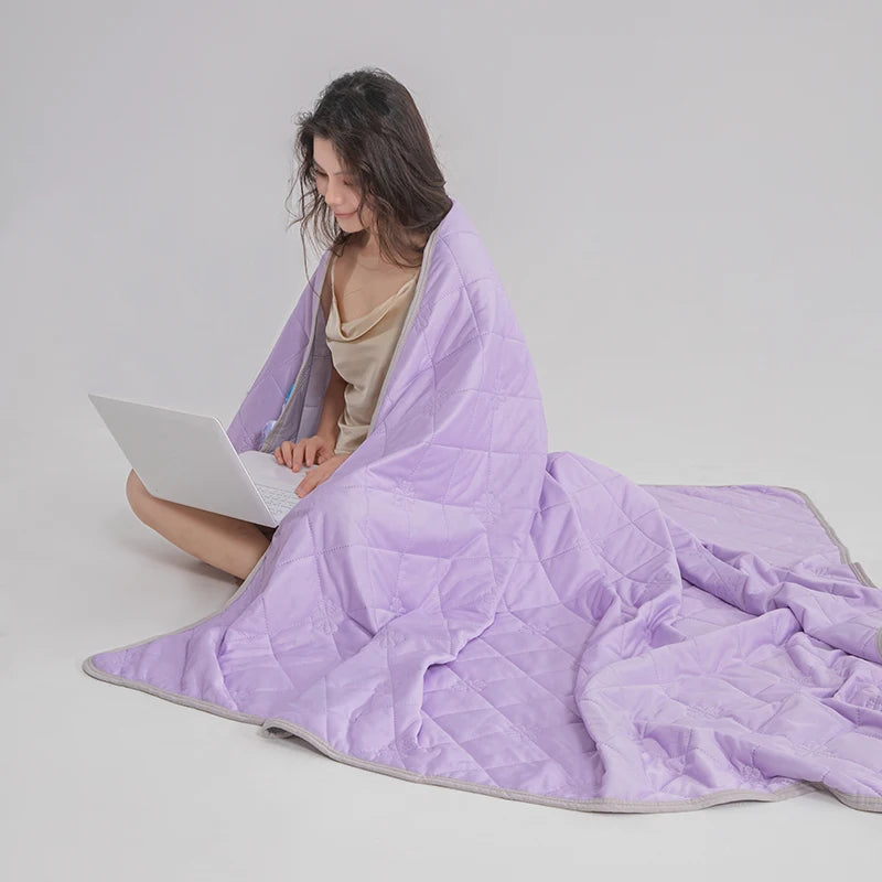 A person is wrapped in a purple quilted blanket, suggesting a cooling breathable blanket for hot sleepers.