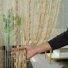 A hand is pulling a sheer gold beaded string curtain down, showing the vertical strands and texture.