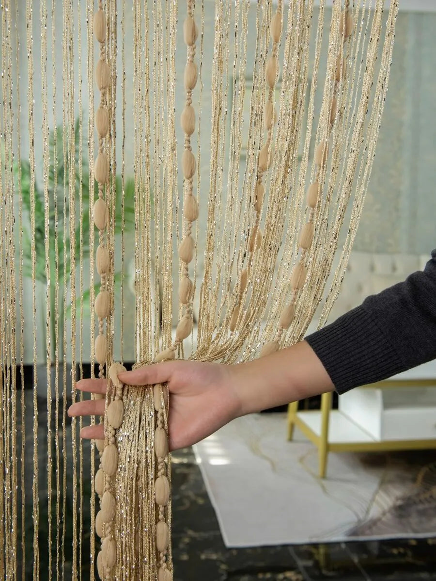 A hand is pulling a long, sheer gold beaded string curtain down, showing the delicate strands and texture.
