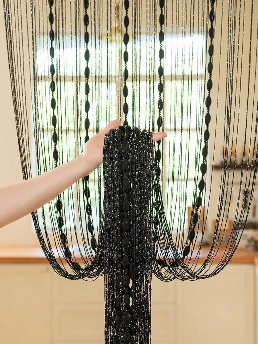 A hand is holding a black beaded string curtain for doorways or weddings.