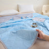 A light blue quilted blanket is spread on a bed, with a hand touching the fabric.