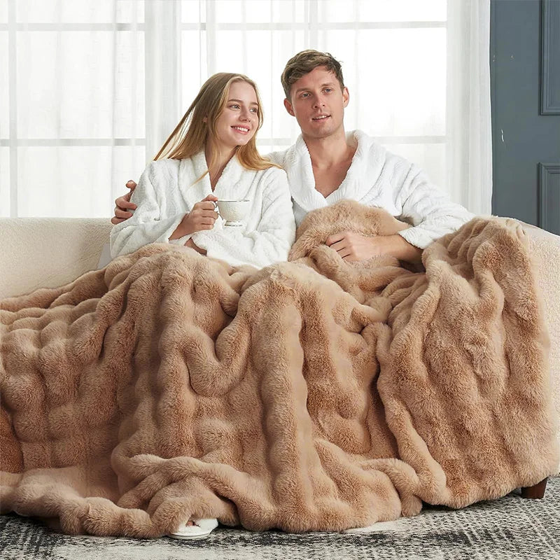 A couple is relaxing together under a large, fluffy tan faux fur rabbit blanket.