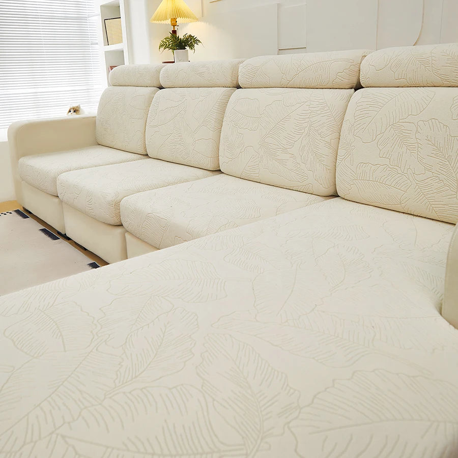 A light beige jacquard elastic sofa cushion cover protecting a sectional sofa in a bright room.