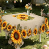 A beige tablecloth decorated with large yellow sunflowers and green foliage outdoors.