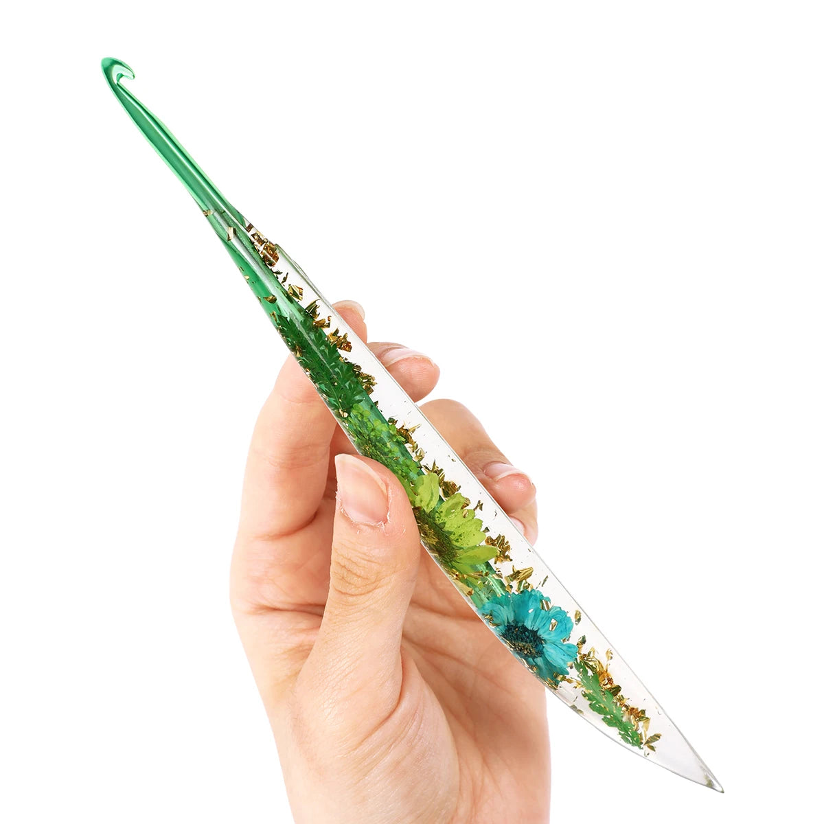 A hand holds a floral patterned epoxy crochet hook set with green and blue accents.