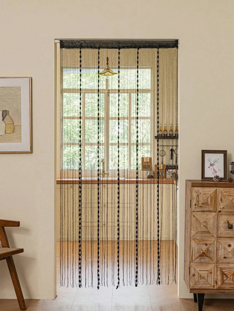 A window dressed with a minimalist beaded string curtain featuring black threads and a gold chandelier.