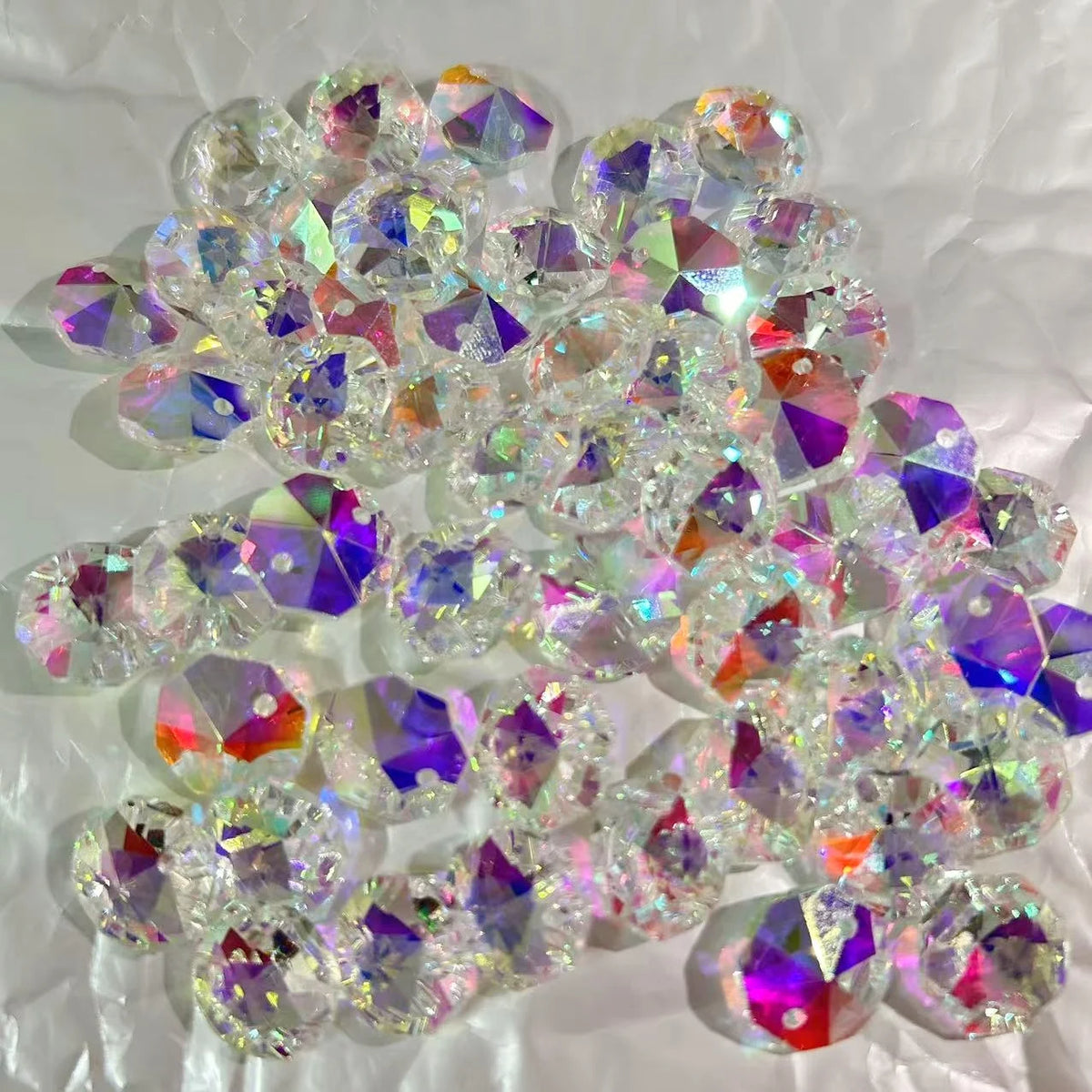 A pile of clear crystal glass beads with two-hole designs showing various iridescent colors.