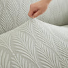 A hand is adjusting a textured, light gray sofa cover featuring a repeating leaf pattern.