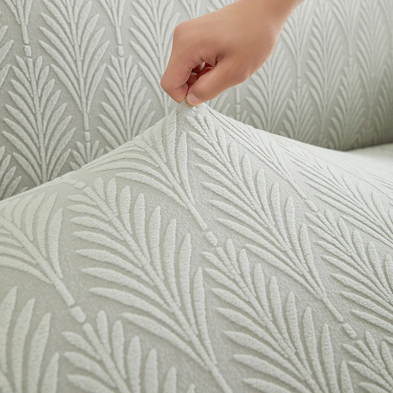 A hand is adjusting a textured, light gray sofa cover featuring a repeating leaf pattern.