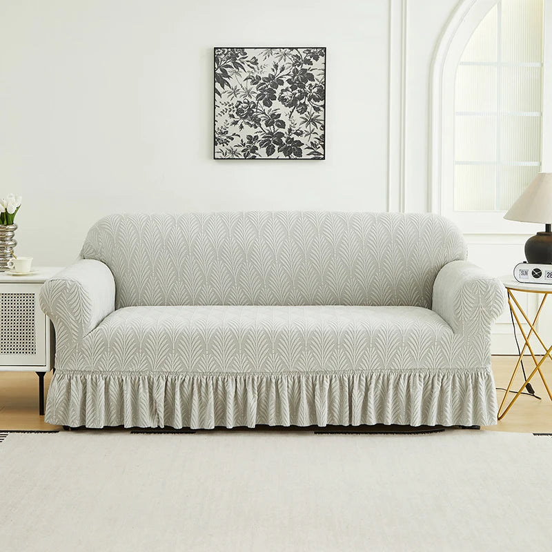 A light gray, ruffled sofa cover is displayed against a white wall with a dark floral print above it.