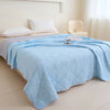 Light blue quilted blanket spread on a bed with white pillows and a cream chair.