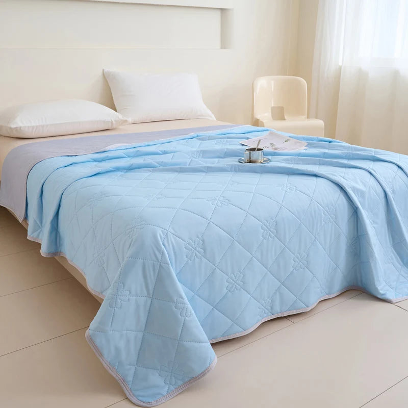 Light blue quilted blanket spread on a bed with white pillows and a cream chair.