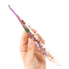 A hand holds a clear epoxy crochet hook with a floral pattern, showing various colors and textures.