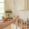 A hand is pulling a long, sheer beaded string curtain down for a doorway or wedding backdrop.