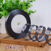 Roll of black satin ribbon with several coils displayed on a wooden board