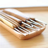 A set of wooden bamboo crochet knitting needles lying on a light wooden surface.
