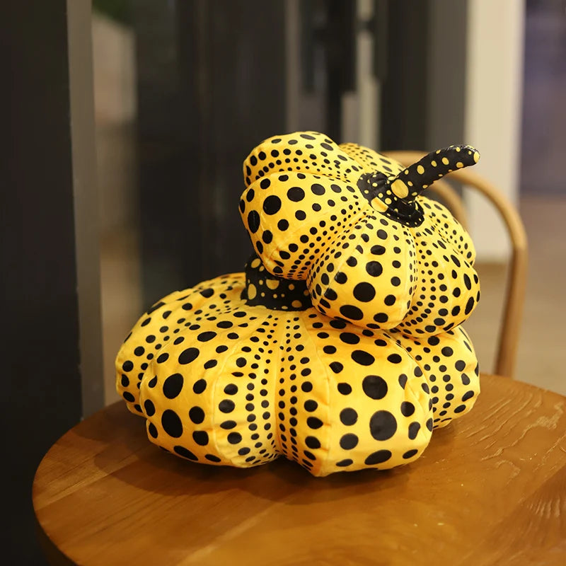 A yellow pumpkin plush cushion covered in black polka dots resting on a wooden surface.
