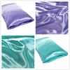 A set of silky satin pillowcases in lavender and teal colors shown folded and draped.