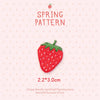 A red strawberry embroidery patch with green leaves on a pink background.