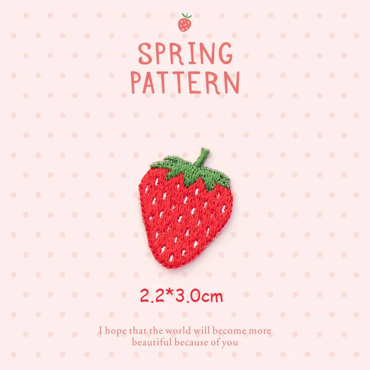 A red strawberry embroidery patch with green leaves on a pink background.