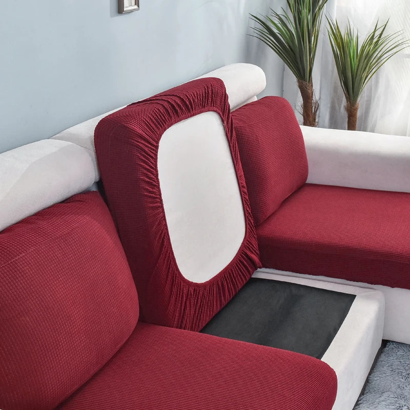 A deep red stretch sofa seat cushion protector slipcover with a white interior and black protective pad.
