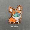 An embroidered patch of an orange fox head wearing a light blue face mask on a gray background.