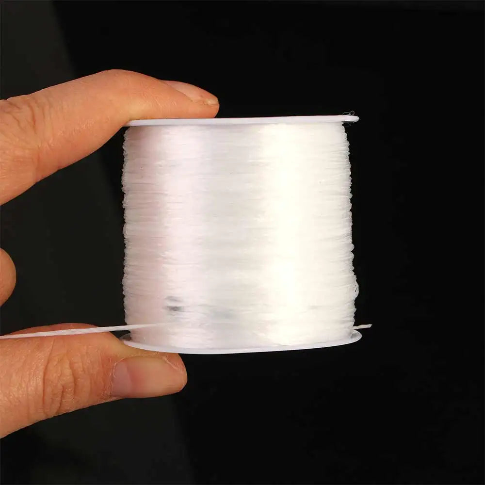 A hand holds a spool of white flat elastic beading thread for jewelry making.