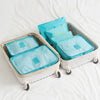 A white clothes storage organizer set with six teal fabric storage boxes is shown on a white bed.